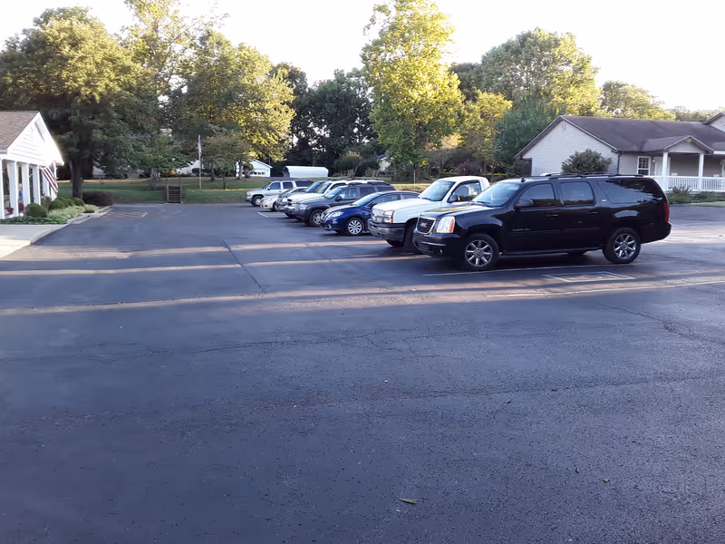 Parking lot with several cars in front of a senior care facility surrounded by trees.