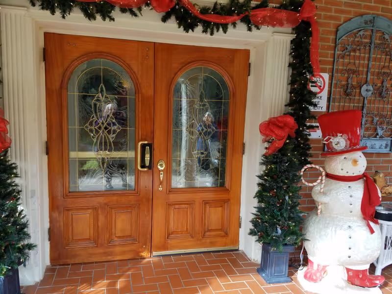 Decorated wooden double doors framed by garlands and a snowman statue at entrance.