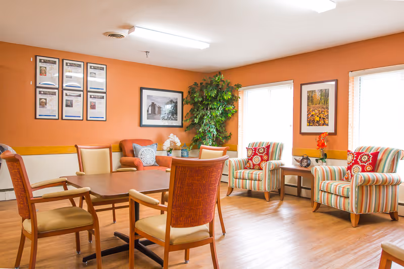 A communal dining and sitting area with a large table, upholstered chairs, and wall art.