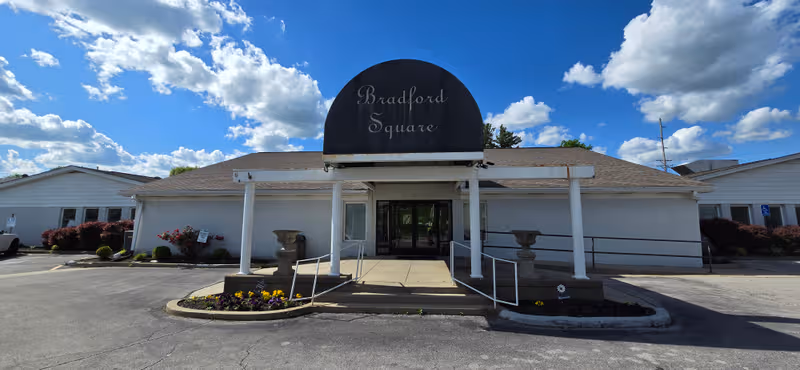 Front view of Bradford Square senior living facility entrance with landscaping and ramp.