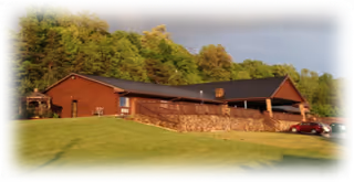 Single-story brick building on a grassy hill with trees behind under a blue sky.