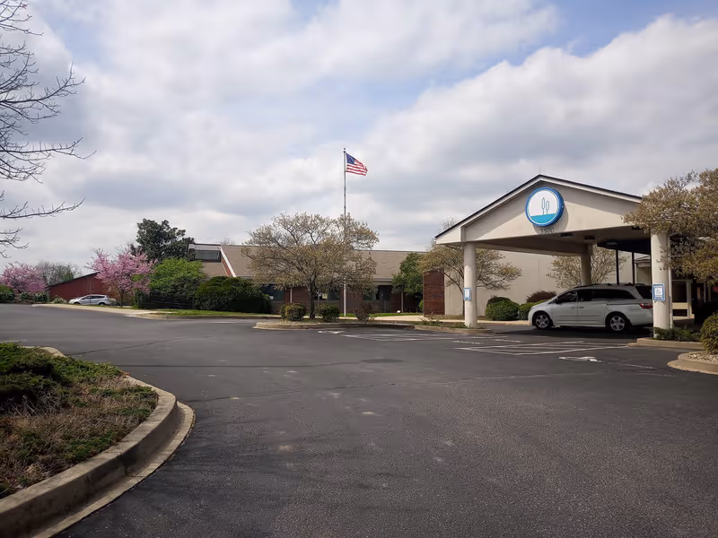 Exterior view of a senior living facility entrance with a covered canopy and parked vehicle.