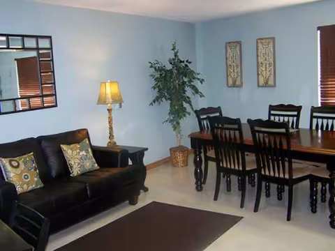 Bright interior living area in a senior facility with sofa, dining table, lamp, and plant.