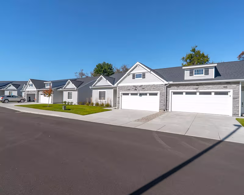 Row of townhome-style senior living buildings with attached garages along a quiet suburban street.