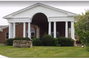 Front exterior view of Windsor Care Center building with white columns supporting a portico entrance, brick walls, and a sign on a large rock that reads 'Windsor Care Center'.