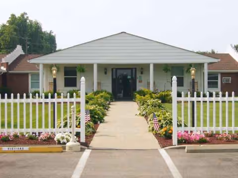 Single-story facility with white picket fence, walkway, and landscaped entrance to Cambridge Nursing & Rehabilitation Center.