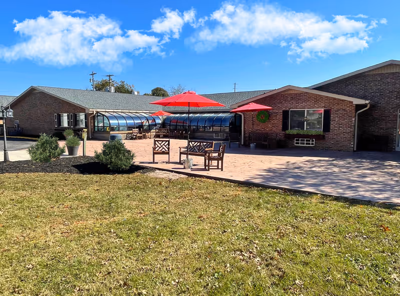 Outdoor patio area of a brick senior living facility with red umbrellas