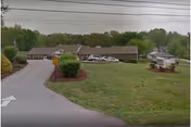One-story senior living facility building set back behind a curved driveway with a grassy lawn, shrubs, and a small sign kiosk.