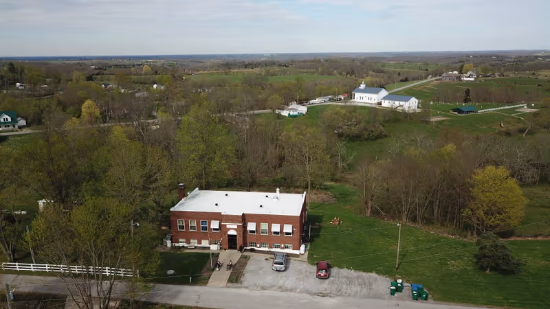 Aerial view of Jonesville Rest Home, a red brick building with white roof amid fields.
