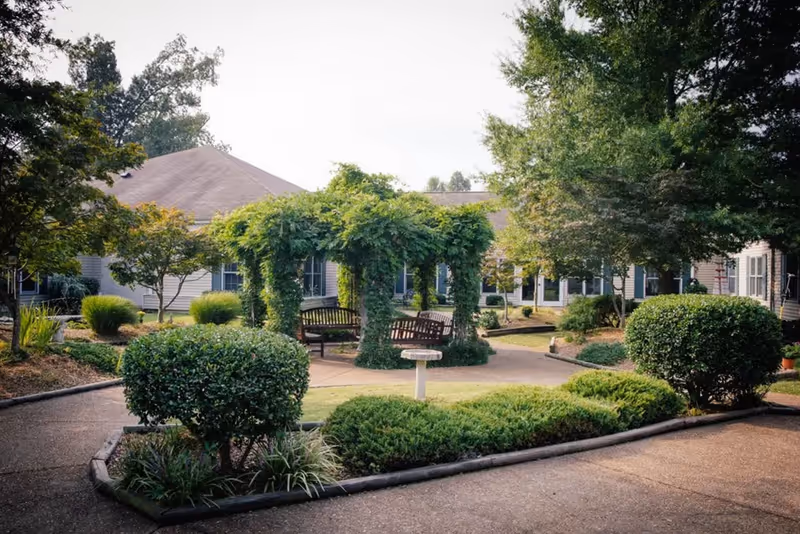 A tranquil courtyard with benches and lush shrubs outside a senior living campus.