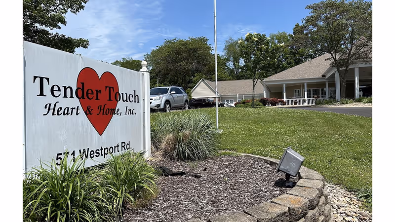 Front entrance of Tender Touch Heart & Home showing the facility sign in a landscaped bed, parked cars, and the building with a covered porch.