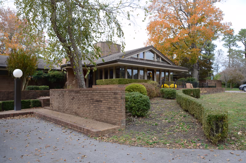 Brick exterior of a senior living facility with a front entrance, trimmed hedges, and autumn trees.