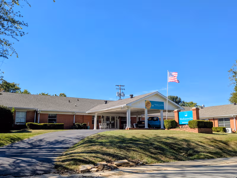 Senior living facility with brick wings, entrance canopy, and American flag in front yard.