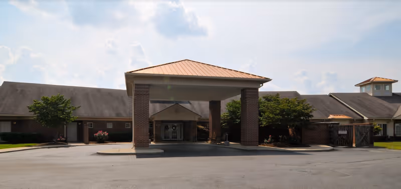 Front entrance of a single-story brick senior living building with a covered porte-cochere and driveway.