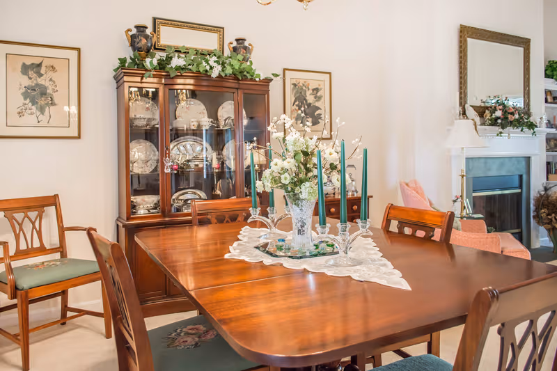 Elegant dining room with wooden table, china cabinet, and floral centerpiece.