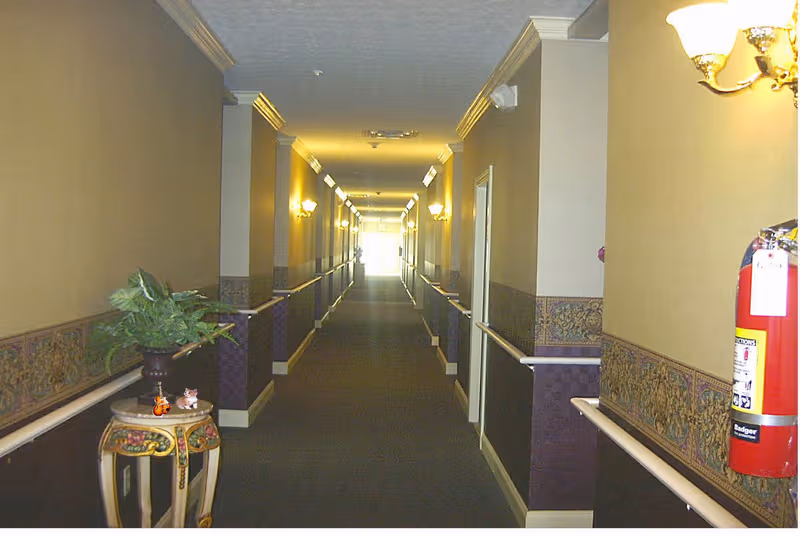 Long hallway inside a senior living facility with beige walls and railings.