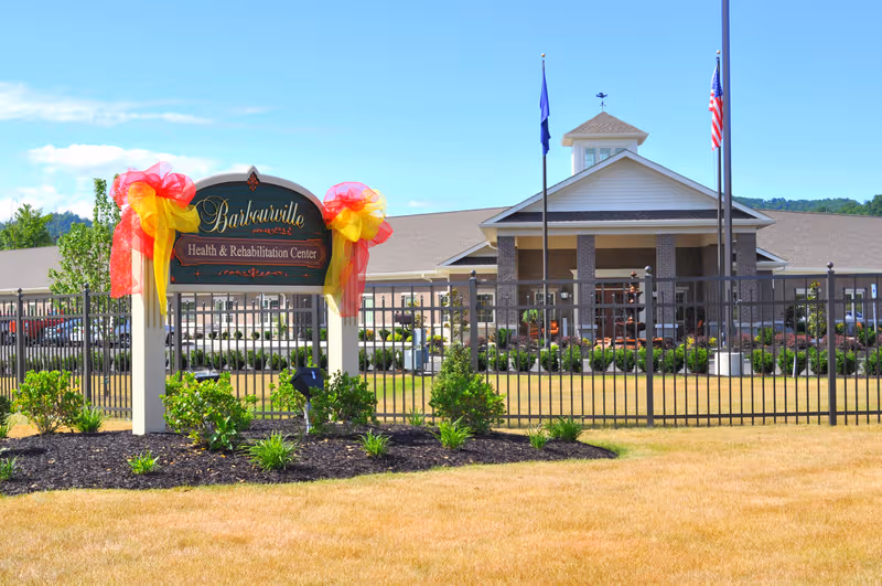 Exterior view of Barbourville Health & Rehabilitation Center with entrance, flags, and sign.