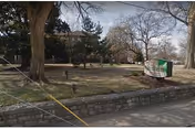 Stone wall and grassy front lawn with trees and a roadside sign reading 'Altenheim' in front of a brick building.