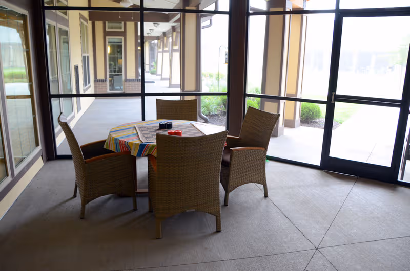 Round table with striped tablecloth and four wicker chairs in a glass-walled outdoor dining space