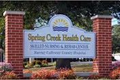 Entrance sign for Spring Creek Health Care Skilled Nursing & Rehab Center mounted between two brick pillars with landscaping and trees behind.