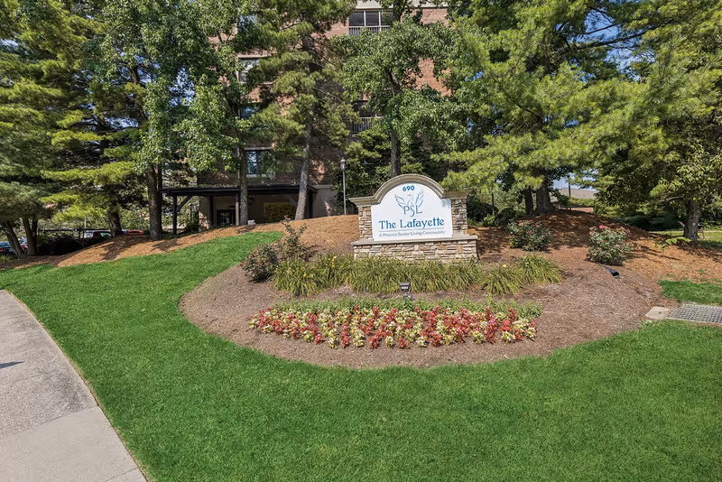The Lafayette senior living community sign sits amid trimmed flower beds and trees at front.