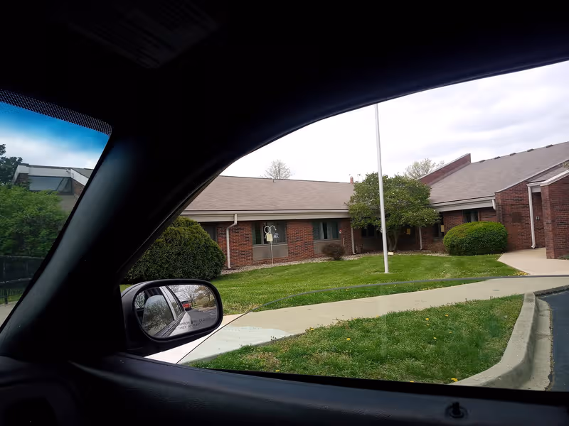 View from inside a car of the Jeffersontown Rehabilitation exterior with lawn and sidewalk.