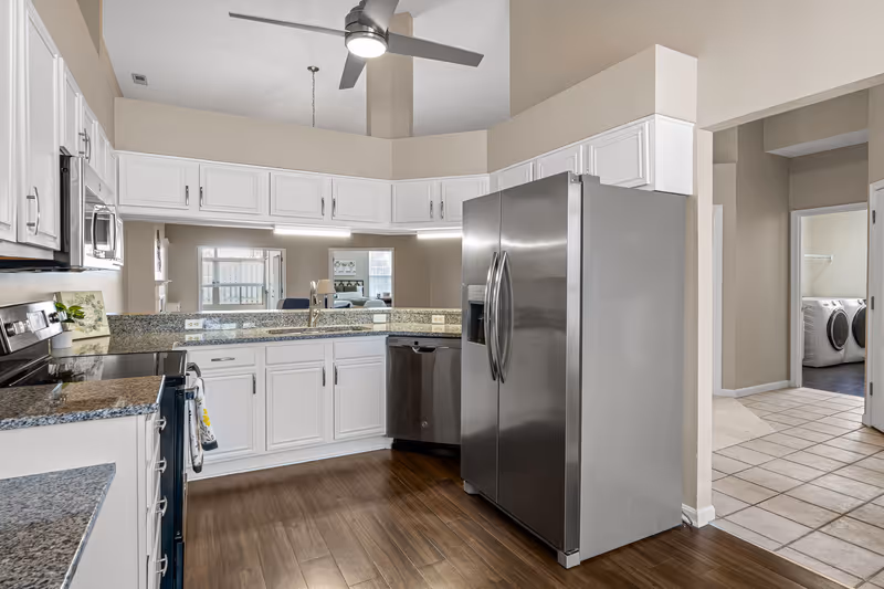 Bright modern kitchen with white cabinets, granite countertops, stainless steel appliances, and a ceiling fan.