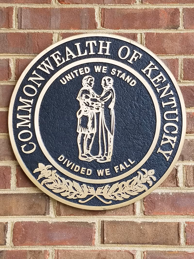 A circular Commonwealth of Kentucky seal plaque is mounted on a brick exterior wall.