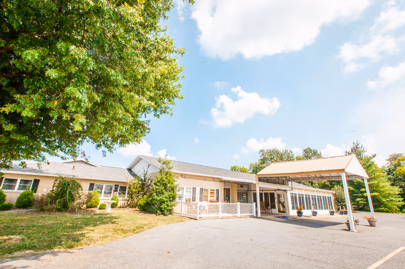 Exterior view of Oakview Nursing and Rehabilitation Center showing a single-story building with a covered entrance, surrounded by greenery and trees under a partly cloudy sky.