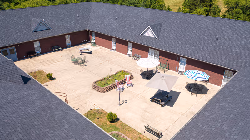 Aerial view of a courtyard in a brick senior living building with tables, umbrellas, and benches.