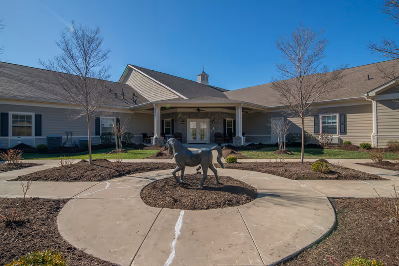 Exterior view of a beige senior living facility with circular driveway and statue