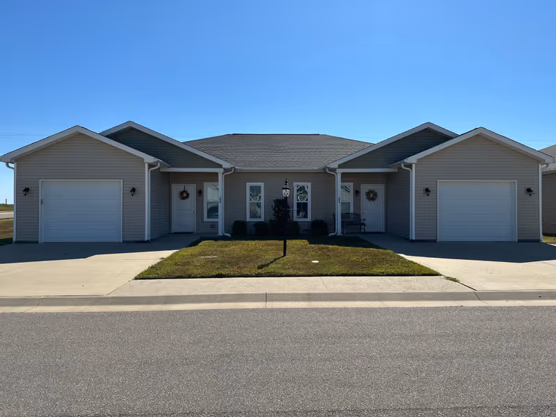 Front exterior of a single-story senior living building with multiple entrances and garages.