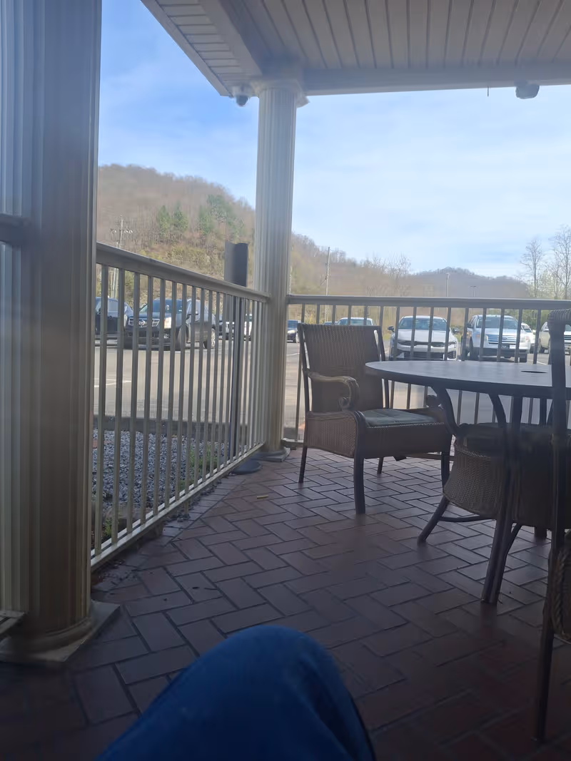 Covered patio with wicker chairs and a round table overlooking a parking lot.