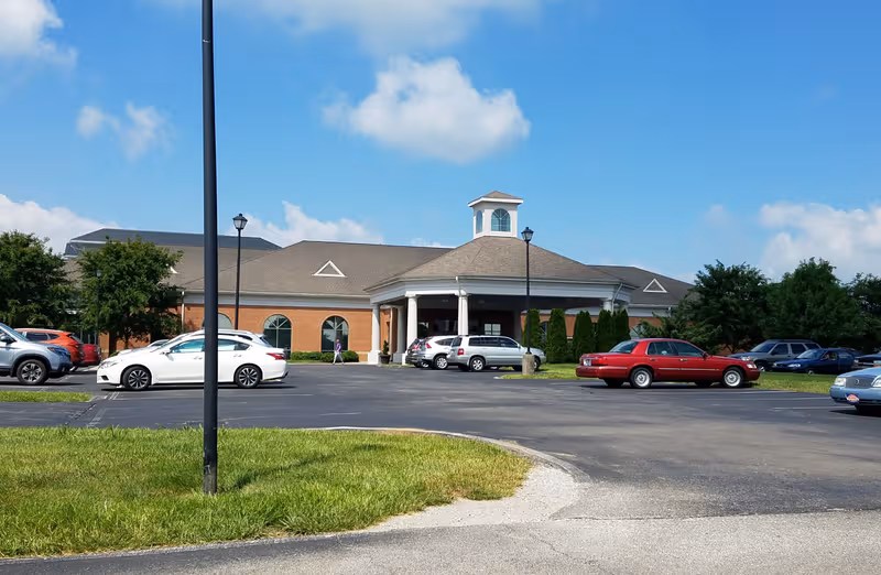 Front view of Wesley Village Senior Living building with a curved driveway and parked cars.