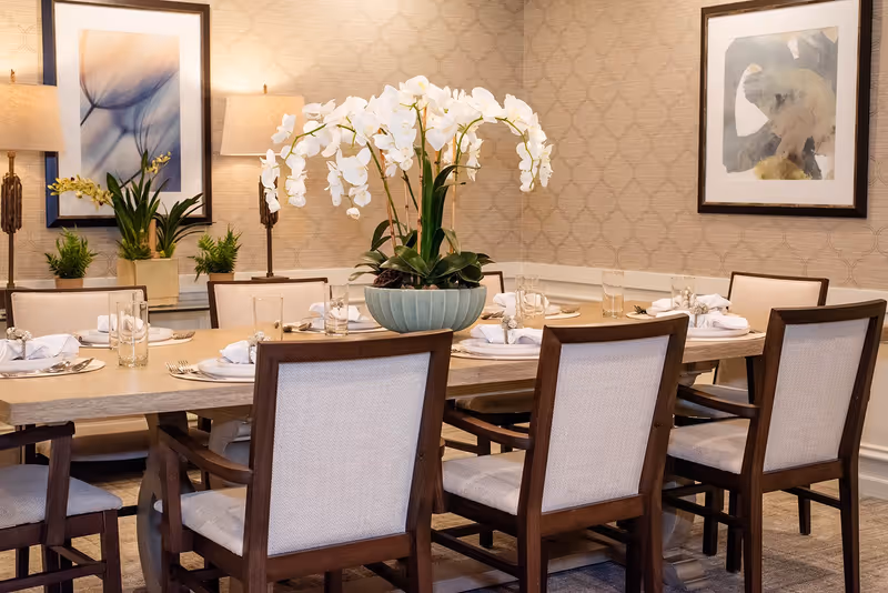 Elegantly set dining table with wooden chairs and a large white orchid centerpiece in a decorated dining room.