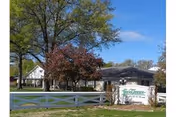 Front exterior of Fern Terrace Lodge building with a white fence, entrance sign, trees, and a blue sky.
