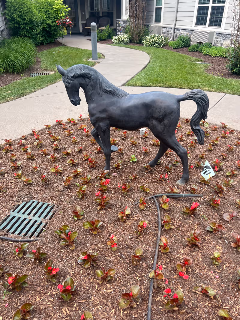 Black horse statue stands in a mulched flower bed near the building entrance.