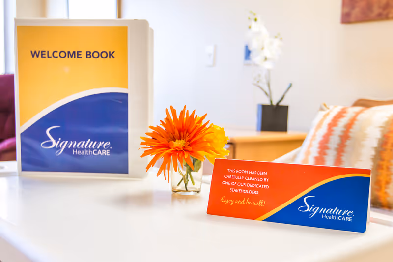 Reception desk with a Welcome Book sign, Signature HealthCARE branding, and an orange flower centerpiece.