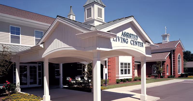 Exterior view of the Franciscan Health Care Center assisted living center building with a covered entrance, white pillars, and a clear blue sky.