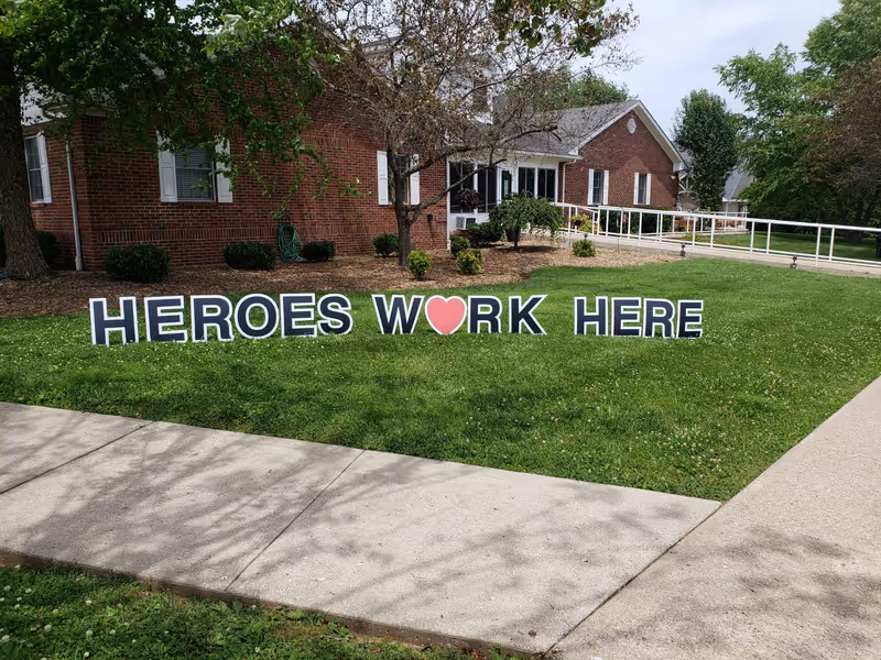 Brick-assisted living facility with a large lawn sign reading HEROES WORK HERE.