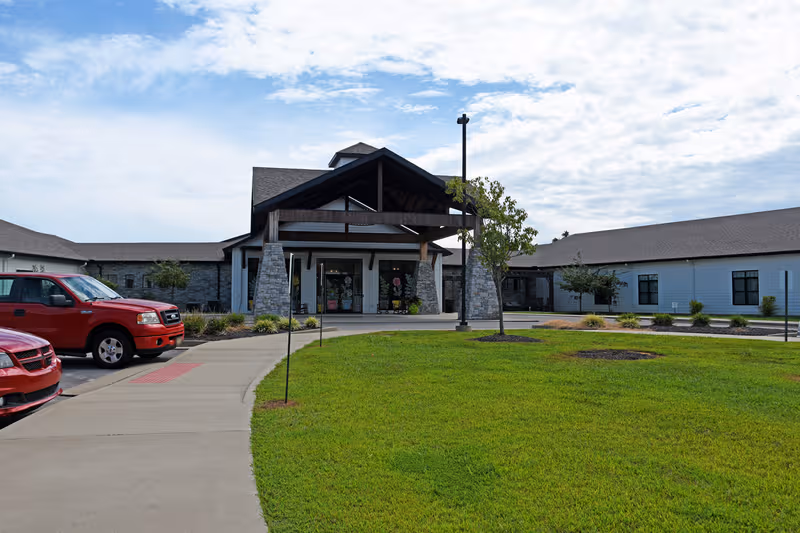 Exterior view of Homeplace of Henderson with entrance, lawn, and parked red vehicles.