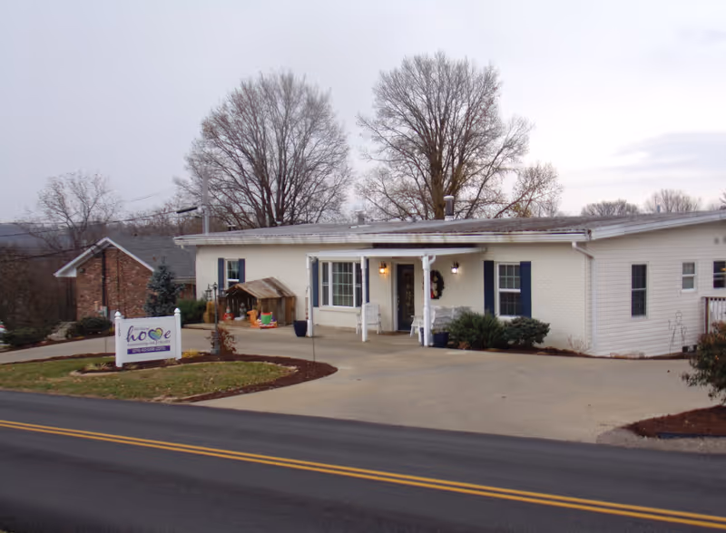 Single-story assisted living facility exterior with sign, entrance, and driveway.