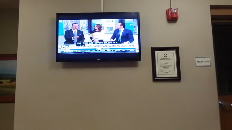 Interior wall in a senior living lobby with mounted TV, framed certificate, and reception sign.