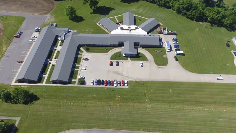 Aerial view of a U-shaped retirement community building with adjacent parking lot and surrounding grassy grounds.
