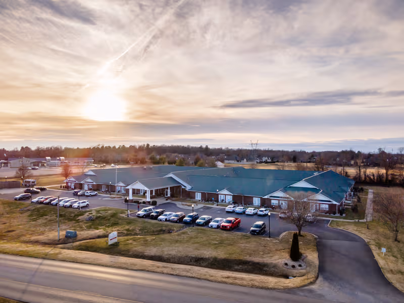 Aerial view of Rivercrest Place senior living facility with parking lot and sunset sky.