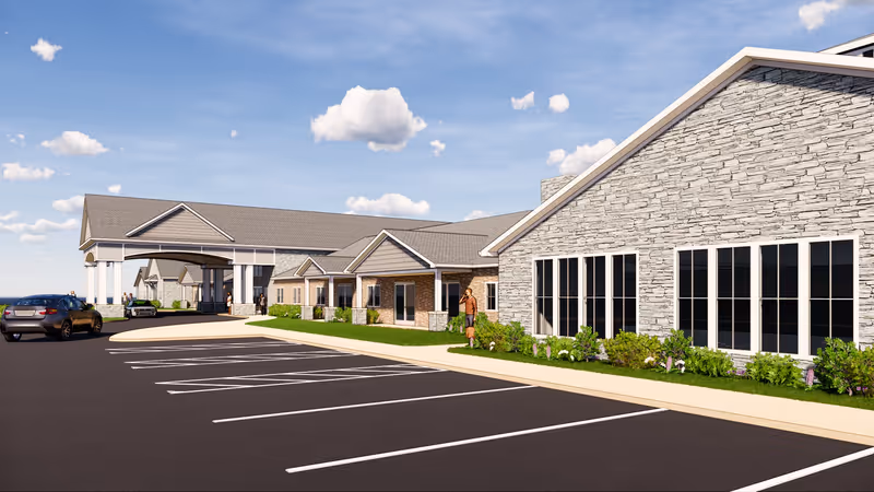 Front exterior of a single-story senior living building with a covered entrance, large windows, landscaping, and a parking lot.