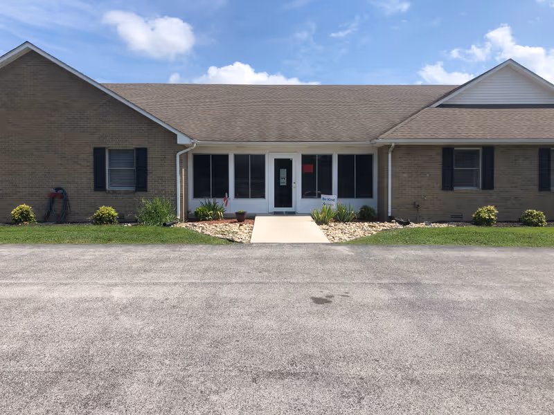 Brick single story senior living facility exterior with central glass entrance and landscaped front walkway.