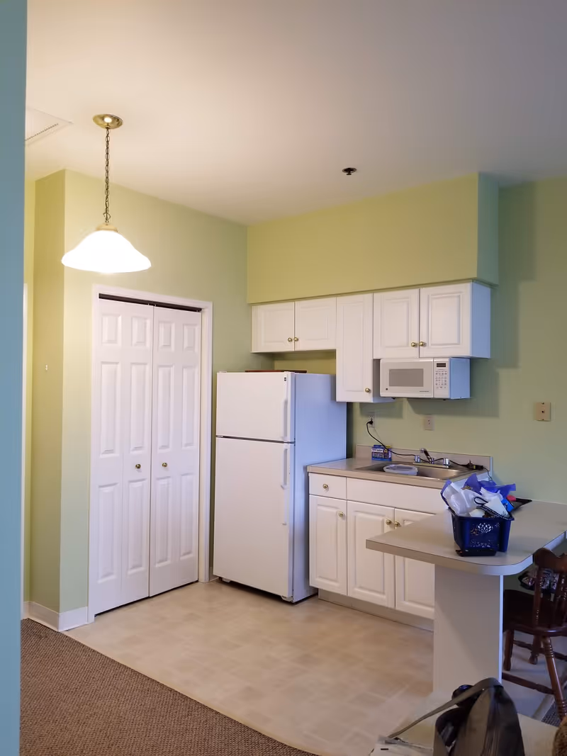 Bright pastel-green kitchen with white cabinets, fridge, microwave, sink, and small counter.