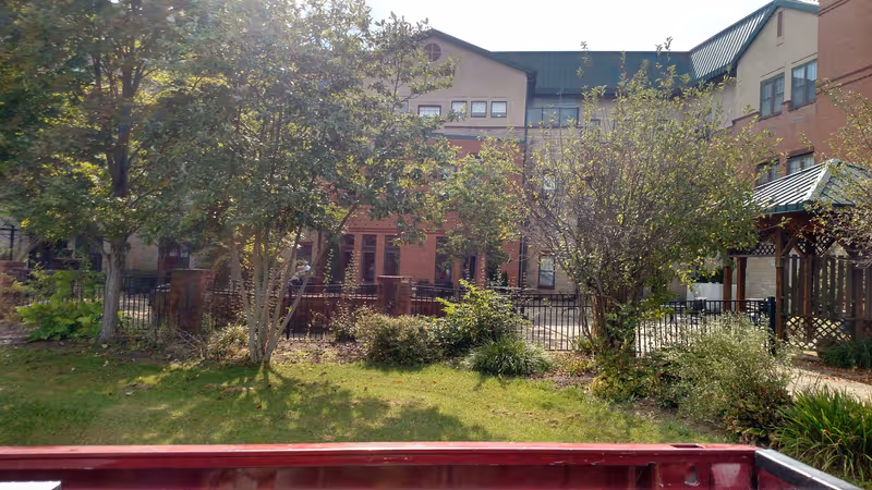 Brick senior living building with a fenced outdoor courtyard and gazebo.