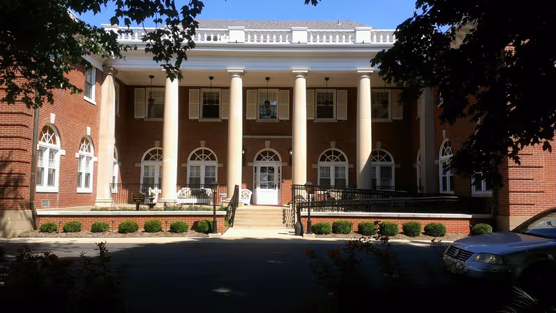 Brick senior living facility with white columns, arched windows, and a front entrance.